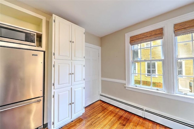 kitchen featuring white cabinetry, stainless steel appliances, a wealth of natural light, and a baseboard heating unit