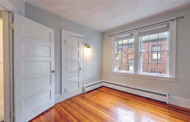 empty room featuring a baseboard radiator, baseboards, and light wood-style floors