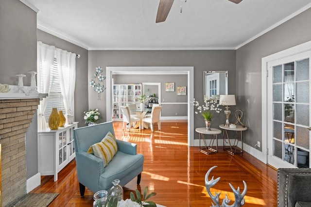 living area with ornamental molding, wood finished floors, baseboards, and ceiling fan