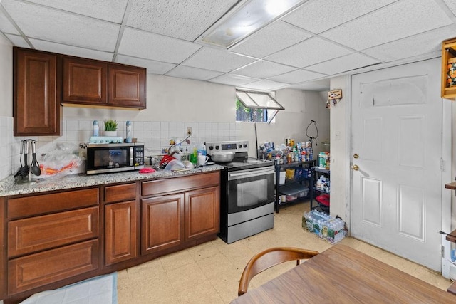kitchen with light floors, light stone countertops, a paneled ceiling, tasteful backsplash, and appliances with stainless steel finishes