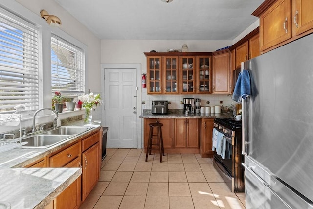 kitchen featuring freestanding refrigerator, brown cabinetry, a sink, and range with gas stovetop