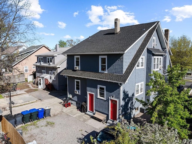 rear view of property featuring a chimney, entry steps, a shingled roof, and fence