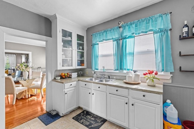 kitchen with a sink, white cabinetry, light countertops, and glass insert cabinets
