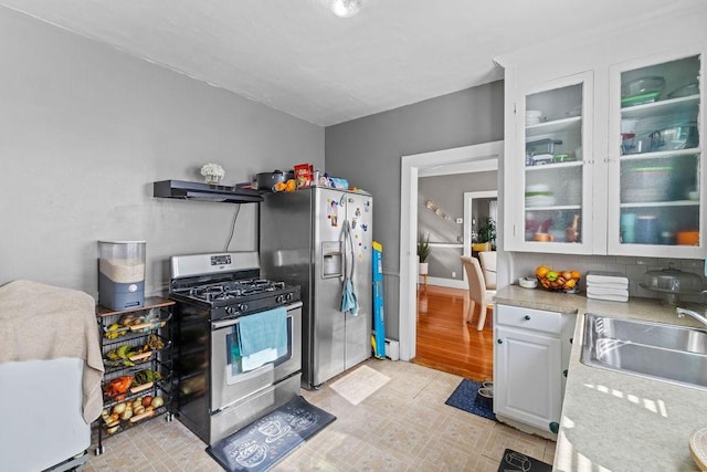 kitchen with a sink, extractor fan, light countertops, glass insert cabinets, and appliances with stainless steel finishes