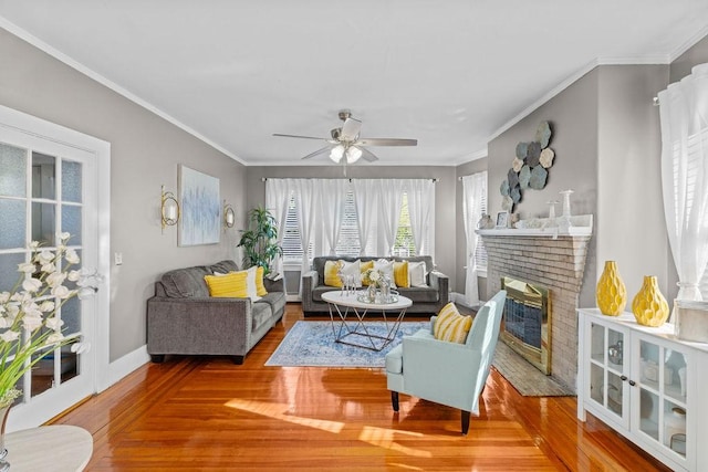 living area featuring a fireplace, crown molding, wood-type flooring, a ceiling fan, and baseboards