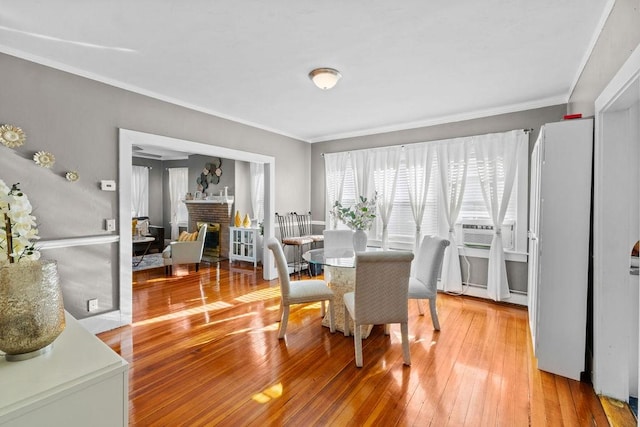 dining space featuring ornamental molding, cooling unit, light wood-style floors, and a brick fireplace