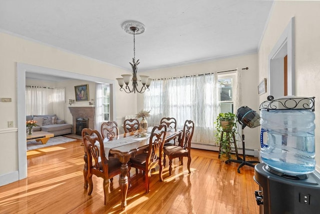 dining area featuring light wood finished floors, a fireplace, a chandelier, and crown molding