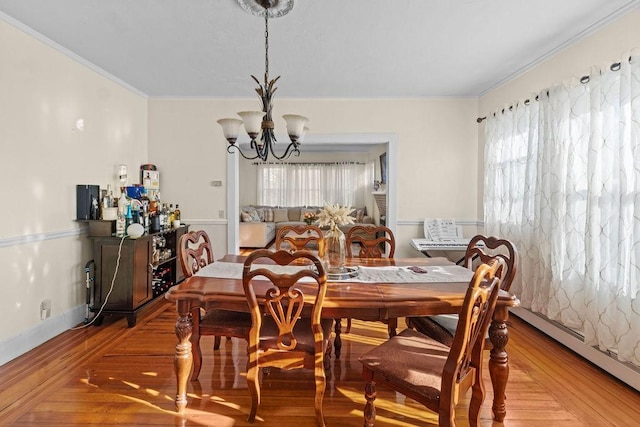 dining space with ornamental molding, a notable chandelier, baseboard heating, and wood finished floors