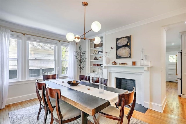 dining room featuring baseboards, ornamental molding, light wood-style flooring, and a fireplace with flush hearth