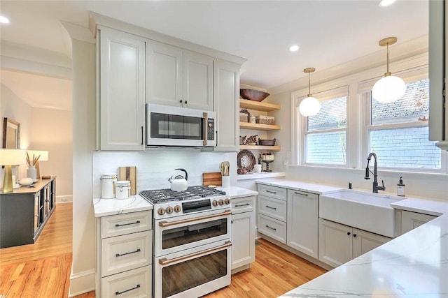 kitchen featuring stainless steel microwave, a sink, decorative light fixtures, light wood finished floors, and range with two ovens