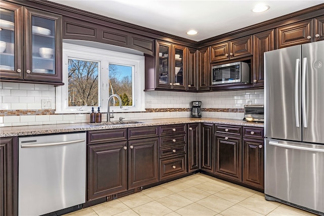 kitchen featuring light tile patterned floors, dark brown cabinets, light stone counters, a sink, and stainless steel appliances
