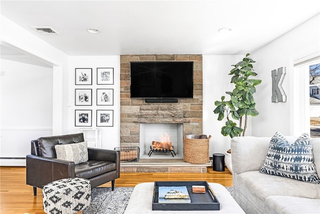 living room with visible vents, wood finished floors, baseboard heating, and a fireplace