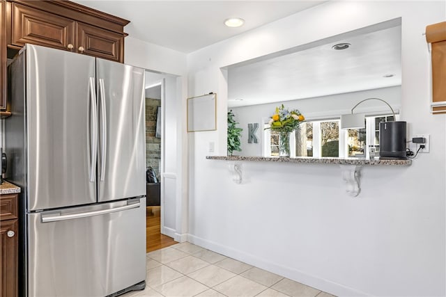 kitchen with freestanding refrigerator, recessed lighting, baseboards, light stone counters, and light tile patterned flooring