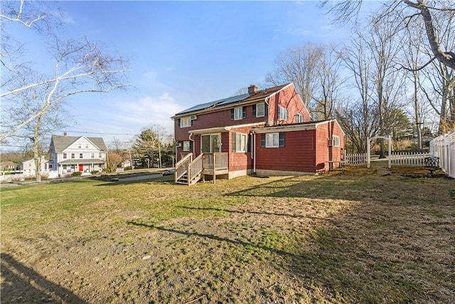 215 Rocky Point Ave, Warwick, RI 02889 - rear view of house with roof mounted solar panels, fence, a chimney, and a lawn