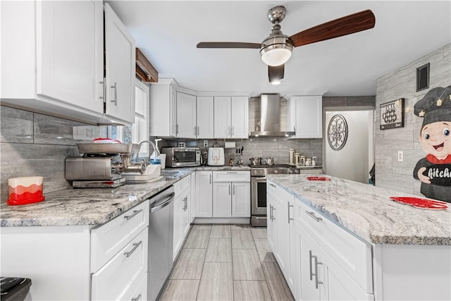 215 Rocky Point Ave, Warwick, RI 02889 - kitchen featuring stainless steel appliances, wall chimney range hood, ceiling fan, white cabinetry, and backsplash