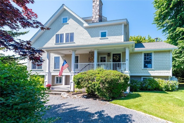 view of front of property with a porch, a shingled roof, a chimney, and a front yard