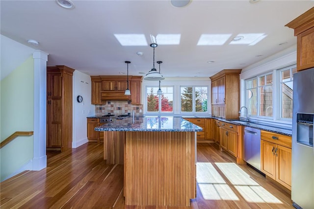 kitchen featuring a kitchen island, decorative backsplash, wood finished floors, dark stone counters, and appliances with stainless steel finishes