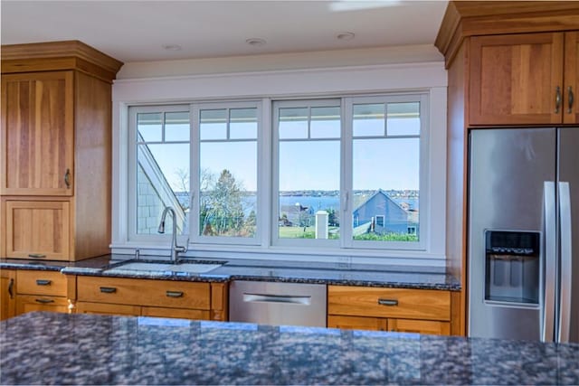 kitchen featuring a sink, brown cabinetry, stainless steel appliances, and dark stone counters