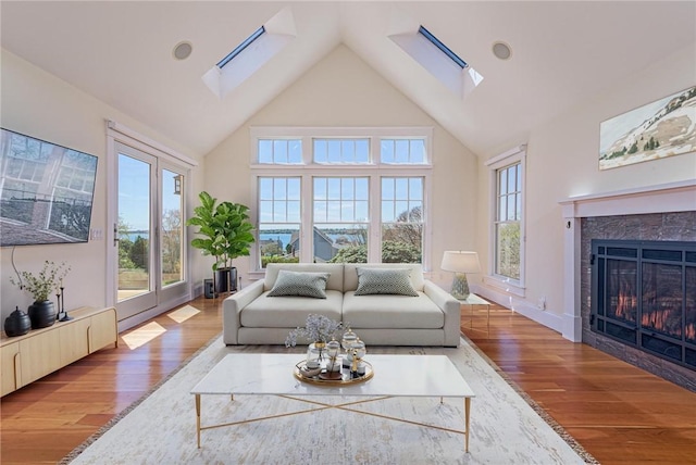 living area with a high end fireplace, high vaulted ceiling, a skylight, and wood finished floors