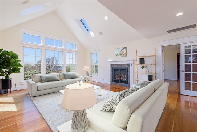 living room featuring a skylight, wood finished floors, high vaulted ceiling, visible vents, and a tiled fireplace