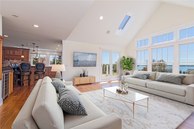 living room with high vaulted ceiling, a skylight, recessed lighting, and wood finished floors