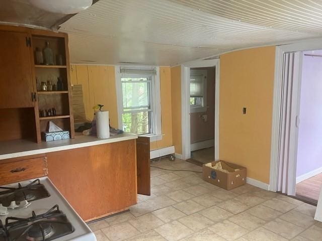 kitchen featuring white gas range oven, brown cabinetry, stone finish floor, baseboards, and baseboard heating