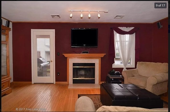 living room featuring a glass covered fireplace, baseboards, visible vents, and wood finished floors