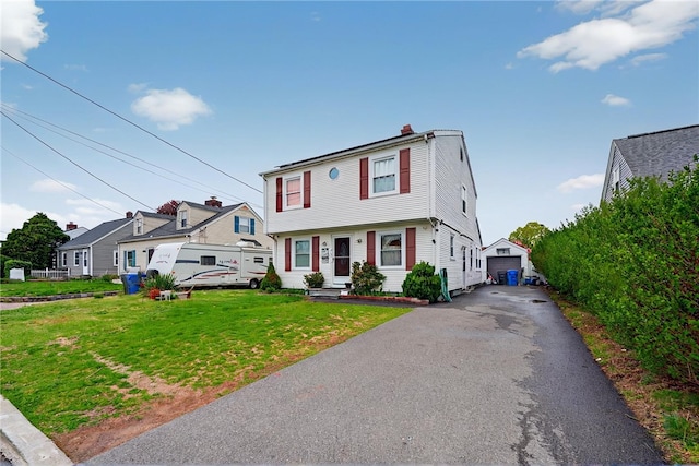 colonial inspired home featuring a chimney, a front yard, an outbuilding, driveway, and a detached garage