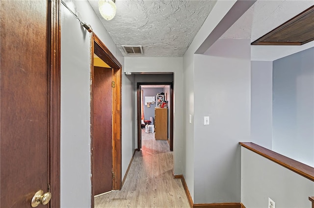 hall with baseboards, light wood-style flooring, visible vents, and a textured ceiling