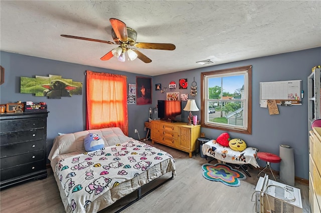 bedroom with a textured ceiling, a ceiling fan, visible vents, and wood finished floors