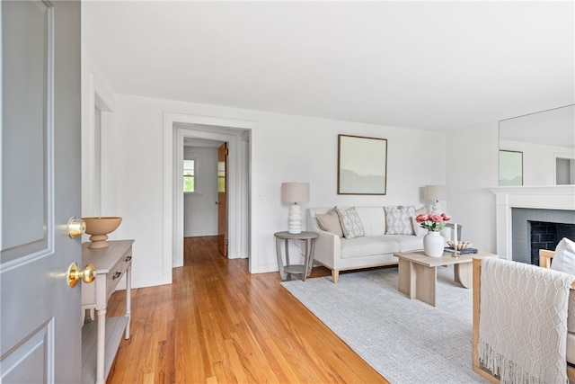 living room with light wood-type flooring, baseboards, and a brick fireplace