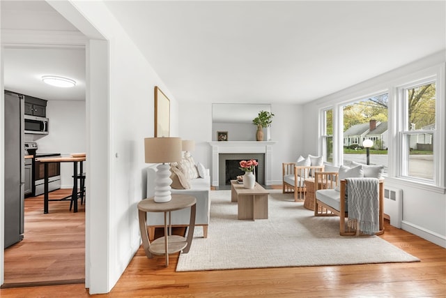 living room featuring baseboards, radiator, light wood-style floors, and a fireplace