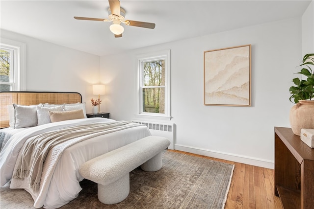 bedroom with baseboards, radiator, multiple windows, and wood-type flooring