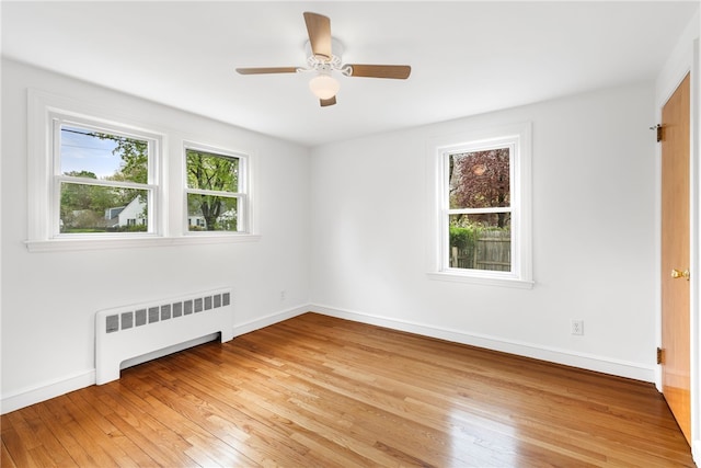 spare room featuring radiator, light wood-style floors, baseboards, and a ceiling fan