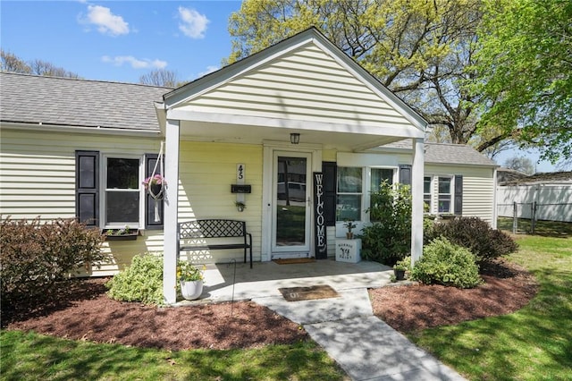 view of exterior entry with covered porch, fence, and a shingled roof