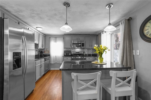 kitchen with a breakfast bar, gray cabinetry, light wood-type flooring, and appliances with stainless steel finishes