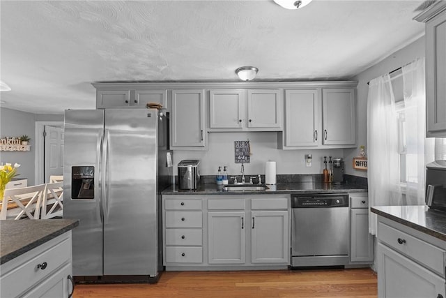 kitchen featuring gray cabinetry, appliances with stainless steel finishes, light wood-style flooring, and a sink