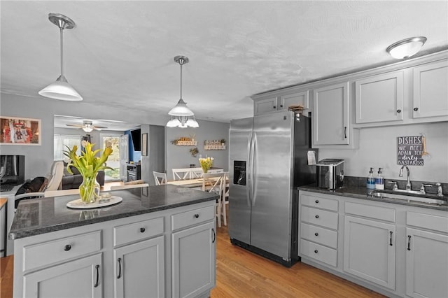 kitchen with a sink, dark stone counters, light wood finished floors, hanging light fixtures, and stainless steel fridge with ice dispenser