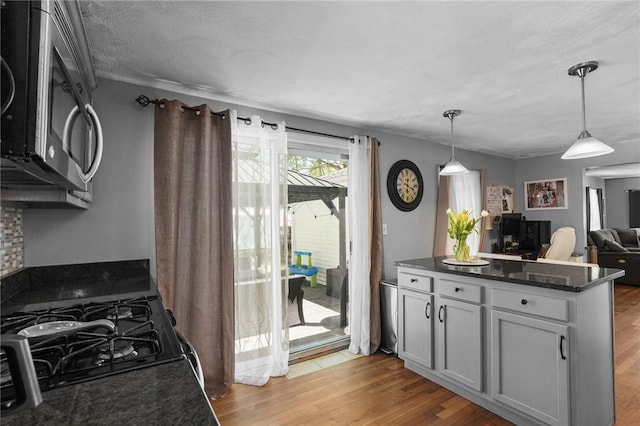kitchen featuring hanging light fixtures, stainless steel microwave, open floor plan, dark stone countertops, and light wood-type flooring