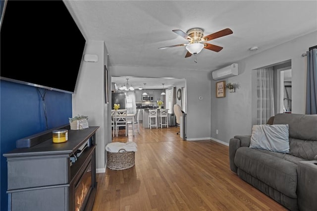 living area with wood finished floors, baseboards, ceiling fan, and an AC wall unit