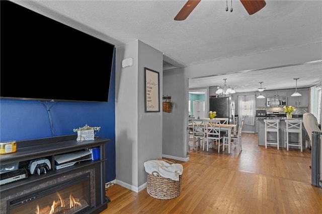living area featuring light wood-type flooring, baseboards, and ceiling fan with notable chandelier