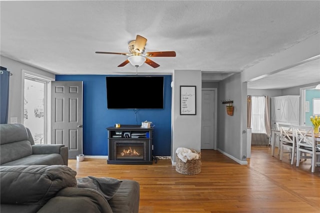 living area with light wood finished floors, a ceiling fan, radiator, a lit fireplace, and baseboards