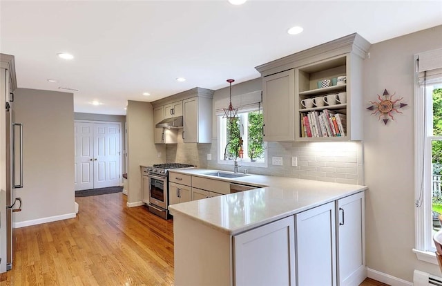kitchen with high end stainless steel range, a sink, under cabinet range hood, light countertops, and a baseboard radiator