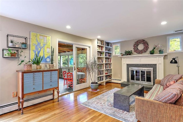 living room with baseboard heating, a glass covered fireplace, wood finished floors, and recessed lighting