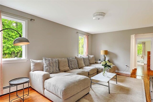 living area with healthy amount of natural light, hardwood / wood-style flooring, baseboard heating, and baseboards
