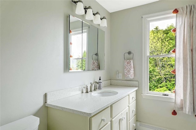 bathroom featuring healthy amount of natural light, toilet, baseboard heating, and vanity