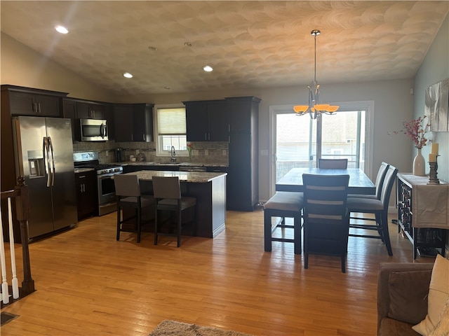 kitchen with a sink, stainless steel appliances, a notable chandelier, decorative backsplash, and a kitchen island
