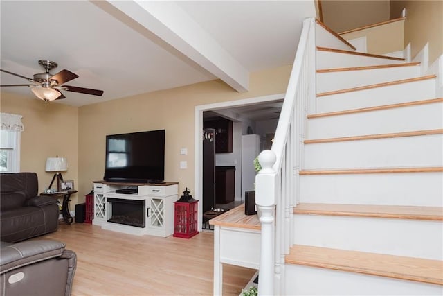living room featuring wood finished floors, beam ceiling, a fireplace, ceiling fan, and stairs