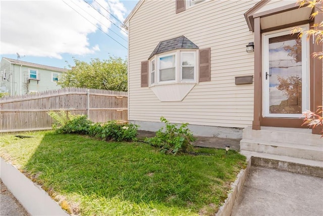 view of property exterior with a yard, fence, and entry steps