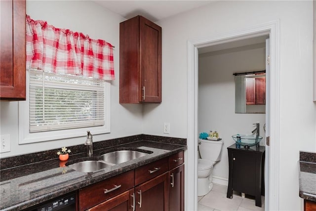 kitchen with dark stone counters, light tile patterned flooring, a sink, and dishwasher